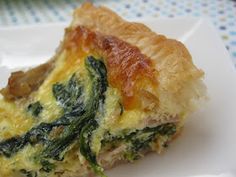 a piece of quiche with spinach and cheese on it sitting on a white plate