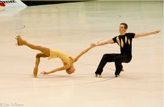 two people in black and yellow dancing on a white floor with one holding the other's hand