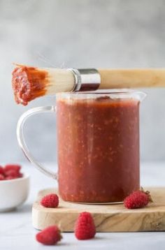 raspberry sauce being poured into a jar with a wooden spatula and small bowl of raspberries in the background