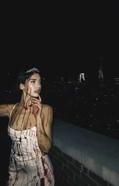 a woman with blood all over her body standing next to a brick wall at night