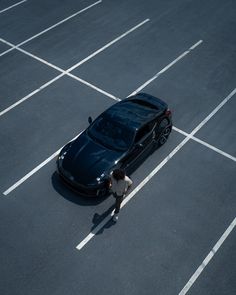 a person standing in the middle of a parking lot next to a black sports car