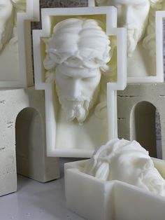 some white sculptures are sitting on a table with frames around them and one is in the shape of a woman's head