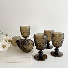 four glass goblets sitting on top of a book next to a white flower