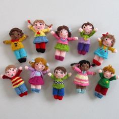 a group of knitted dolls sitting next to each other on a white surface with their hands in the air