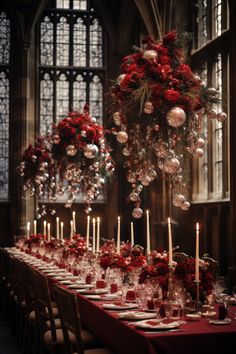 a long table is set with candles and red flowers in front of the windows, surrounded by hanging ornaments