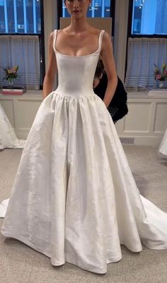 a woman in a white wedding dress standing next to a window