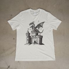 Unleash the magic of fantasy and dark art with this Dragon Vintage Dark Art Graphic T-Shirt, a stunning blend of retro 90s tattoo style and medieval Y2K aesthetics. Featuring a fierce dragon perched atop a detailed medieval castle, this shirt captures the essence of grimdark fantasy and is perfect for dragon lovers and fans of bold, edgy designs. Whether you're looking to complete your baggy vintage wardrobe, gift a unique piece to a fellow dragon enthusiast, or stand out with a dreamy, abstract art-inspired tee, this shirt offers the perfect mix of style and comfort. Ideal for casual wear, cosplay events, or as a statement piece for fantasy and tattoo art lovers alike. Why You'll Love It: Unique Design: Intricate dragon and medieval castle graphic with dark art vibes. Versatile Style: Ret Dragon Perched, Fantasy Shirt, Y2k Tattoo, Fierce Dragon, Vintage Dragon, Baggy Style, Dragon Lover, Vintage Wardrobe, Medieval Castle