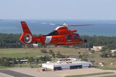 a red helicopter flying over an airport near the ocean