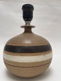 a brown and white striped vase with a black top sitting on a table in front of a white background