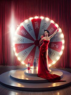 a woman in a red dress standing next to a giant wheel of fortune on stage