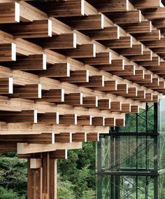 the inside of a building with wooden beams and glass walls on both sides, along with trees in the background