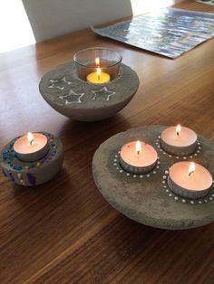 four lit candles sitting on top of a wooden table next to two bowls filled with rocks