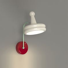 a red and white light hanging from the side of a gray wall next to a lamp