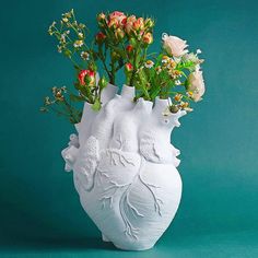 a white vase with flowers in it on a green tableclothed surface, against a teal background