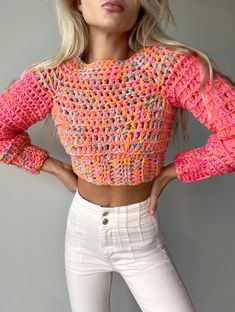 a woman with blonde hair wearing white pants and a pink crochet sweater is posing for the camera