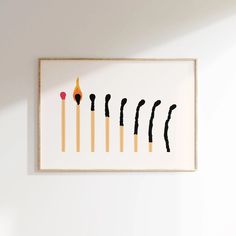 a white wall with a framed print of matches and matchsticks in different shapes