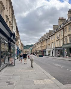 people are walking down the sidewalk in front of shops on a cloudy day with blue skies