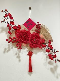 red flowers and leaves are hanging on a white wall with a chinese style sign in the background