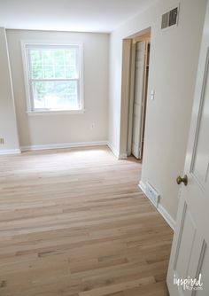 an empty room with hard wood flooring and a door to another room in the background