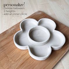 a wooden cutting board topped with three white flower shaped bowls on top of each other