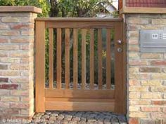 a wooden gate with brick pillars and a metal mailbox on the side of it