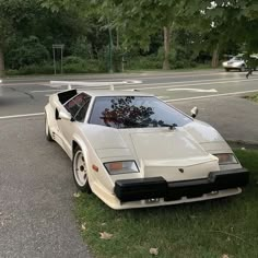 a white sports car parked in the grass next to a street with trees and bushes