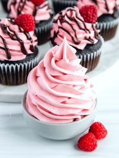 several cupcakes with pink frosting and raspberries on a white plate