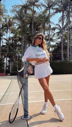 a woman standing on a tennis court with a racket in her hand and palm trees behind her