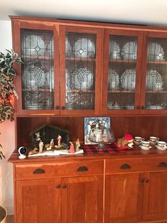 a wooden china cabinet with glass doors and drawers on it's sides, next to a potted plant