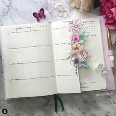 an open notebook with flowers on it next to a pen and flower clippings