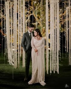 a man and woman standing in front of a tree with white streamers hanging from it