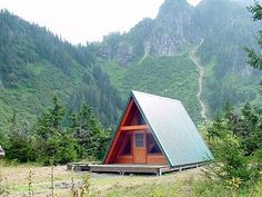 there is a small cabin in the middle of some trees and grass with mountains in the background