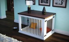 a white dog crate with orange and yellow pillows on it in front of a blue wall