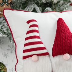 two red and white christmas pillows with santa's hats on them next to a pine tree