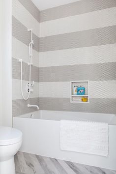 a white bathroom with grey and white stripes on the walls, toilet and bathtub