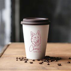 a coffee cup sitting on top of a wooden table with coffee beans scattered around it