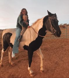 a woman riding on the back of a black and white horse next to a baby