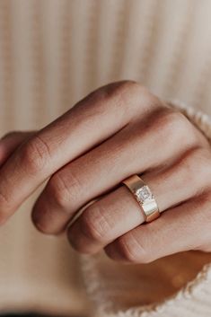 a woman's hand wearing a gold wedding band with a diamond in the middle