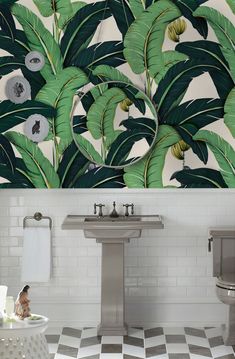 a bathroom with white tile and green leaves on the wall behind it is a pedestal sink