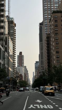 an empty city street with tall buildings in the back ground and cars driving down it