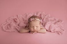 a baby girl sleeping on a pink blanket with her hands under her chin and eyes closed