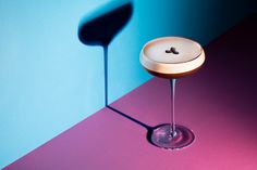 a martini glass sitting on top of a table next to a blue and pink wall