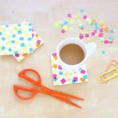 a cup of coffee sitting on top of a table next to scissors and paper clips