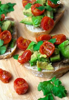 slices of bread with avocado, tomatoes and cilantro on them sitting on a cutting board