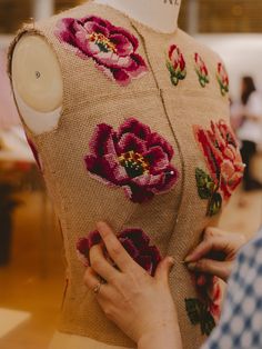 a woman is working on a dress made out of fabric with flowers and leaves embroidered on it