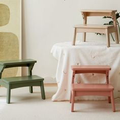 two small wooden stools sitting next to each other in front of a white bed