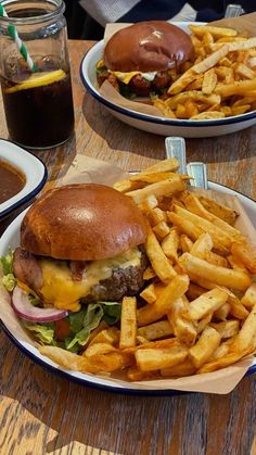 two plates with hamburgers and french fries are on the table next to some drinks