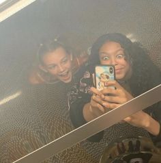 two young women taking a selfie in front of a mirror with their cell phone