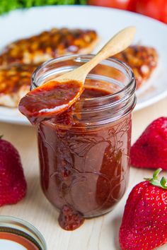 a jar of strawberry jam next to some sliced strawberries on a white plate with a wooden spoon