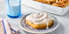 a cinnamon roll with icing on a plate next to a glass of milk